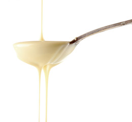 Condensed milk pouring from a spoon, isolated on white