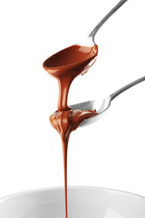 Melted milk chocolate pouring from spoons, isolated on white