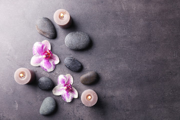 Fototapeta na wymiar Relax concept - composition of aroma candles with pebbles and flower on grey background
