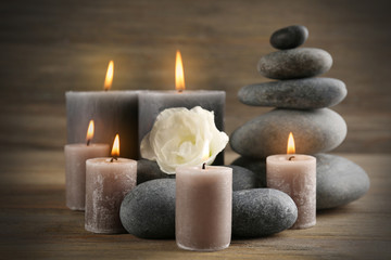Fototapeta na wymiar Alight wax grey candle with pebbles and beautiful flower on wooden background