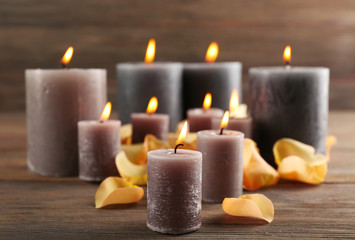 Obraz na płótnie Canvas Alight wax grey candle with flower petals on wooden background
