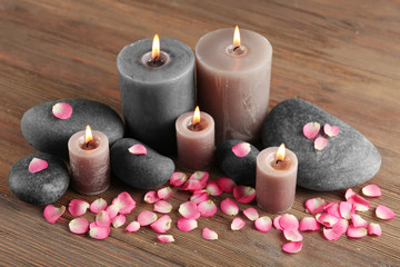 Obraz na płótnie Canvas Alight wax grey candle with flower petals and pebbles on wooden background