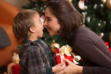 Young mother and her cute little son sharing Christmas presents in front of the Christmas tree