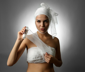 Young playful woman with a gauze bandage on her head and chest, on grey background