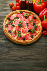 Tasty pizza with salami and red vegetables on wooden background, copy space