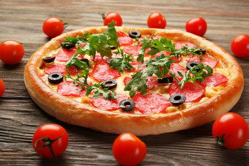 Tasty pizza with salami decorated with tomatoes on wooden background, close up