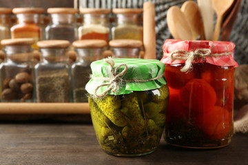 Jars with pickled vegetables and beans, spices and kitchenware on wooden background