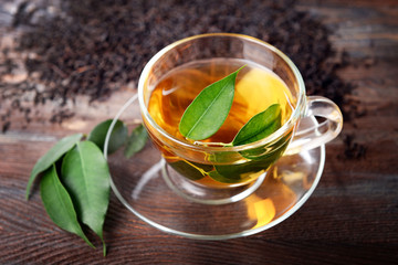 Glass cup of tea with green leaves on wooden background decorated with scattered tea