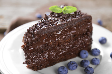 Chocolate cake with chocolate cream and fresh blueberries on plate, on wooden background