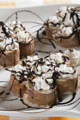 Rolls of brown crepes with sweet filling served on a white plate with tiramisu cream, chocolate and whipped cream. 