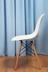 Stylish white chair on blue curtains background