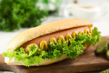 Tasty hot-dog with vegetables on wooden chopping board, close up