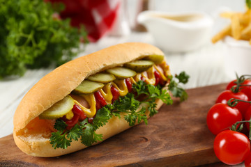 Delicious hot-dog with tomatoes  on wooden chopping board, close up