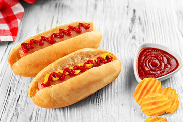 Delicious hot-dogs with chips on white wooden background