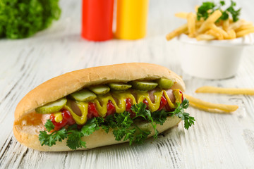 Delicious hot-dog with French fries and vegetables on white wooden table