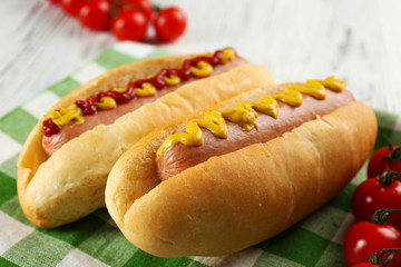 Delicious hot-dogs with tomatoes on green checkered cotton napkin, close up