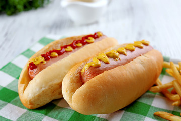 Delicious hot-dogs with French fries on green checkered cotton napkin, close up