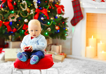 Obraz na płótnie Canvas Funny baby sitting on sledge and Christmas tree and fireplace on background