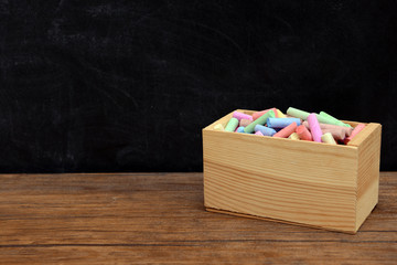 Wooden box of coloured chalk in front of blackboard