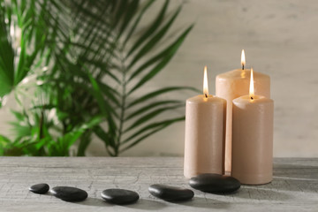 Fototapeta na wymiar Spa composition of candles, stones and green leaves on light background