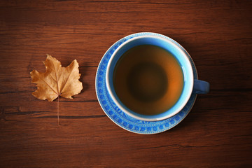 Cup of tea with autumn leaf on wooden table.