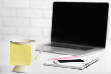 Yellow adhesive note on coffee cup, on laptop background