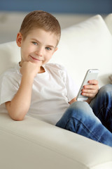 Little boy with mobile phone sitting on a sofa at home