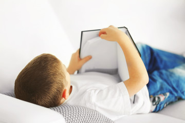 Little boy reading book on a sofa at home