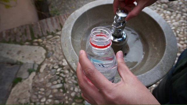 Human filling empty plastic bottle with public drinking fountain in Spain