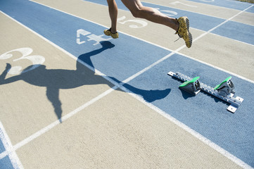 Athlete in gold shoes sprinting from the starting blocks over the starting line of a race on a blue and tan running track 