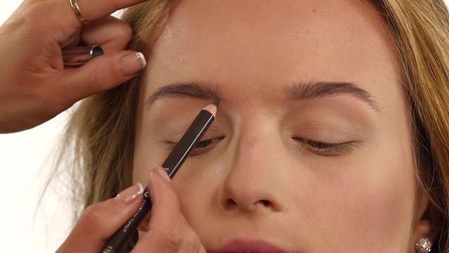 Beautiful woman draw beauty shape of eyebrows using cosmetic brush. Close up. Slow motion