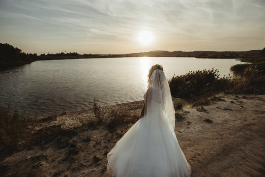 bride looking at the amazing sunset on a background of beautiful sunny lake and sand