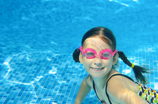 Child swims in pool underwater, happy active girl in goggles has fun under water
