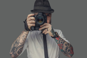 A man with tattooes on arms holding dslr photo camera.