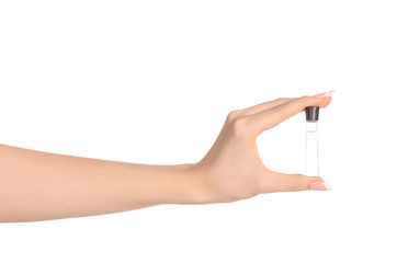 Perfume and body care theme: beautiful female hand holding a small transparent bottle of perfume on a white background isolated