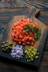 Rustic wooden chopping board with salmon tartar, high angle view