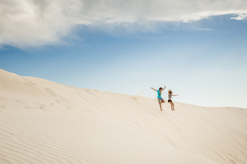 Boy and girl jumping in sand dunes, Green Head, Western Australia, Australia