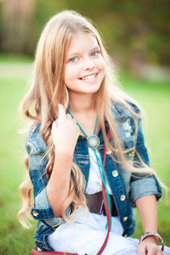 Smiling blonde teen girl 12-15 year old wearing denim jacket and white rustic style outdoors. Looking at camera. Childhood. 