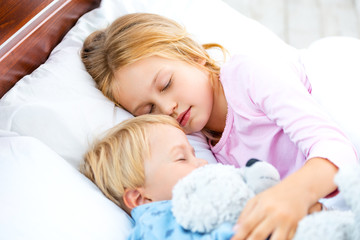Little girl and boy sleeping on white bed