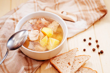 healthy hot lunch , chicken soup with potatoes , carrots , chicken breast , spices and rye bread on a wooden background