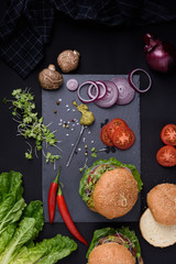 Closeup of homemade burgers with fresh vegetables on slate board. Healthy food still life, top view.