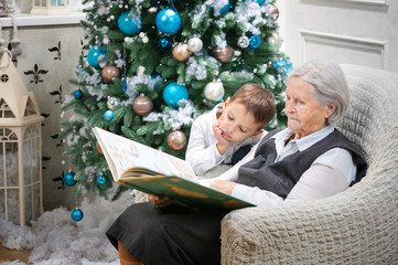 Senior woman reading a book to her grandson beside a Christmas tree