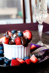 White ramekin lemon dessert topped with melted chocolate fresh strawberries and blueberries and sprinkled with powdered sugar