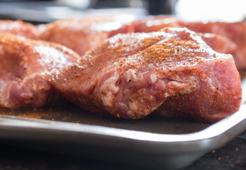 Closeup of uncooked pork chops being prepared on a baking sheet for grilling