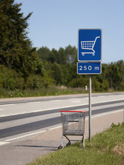 abandoned shopping cart at the limited-access road sign. concepts: consumption crisis, absurd, wtf,...