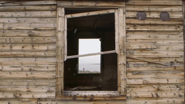 Expeditioner seen through the window of an abandoned house in Hebron, Newfoundland and Labrador on a snowy day. Slow Motion