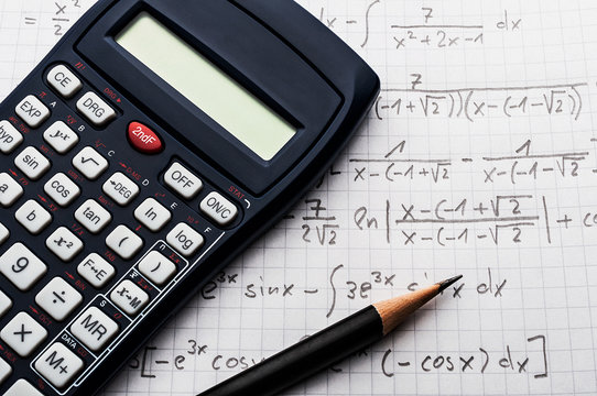 Maths concept - handheld calculator and pencil over a sheet of paper with maths-formulas