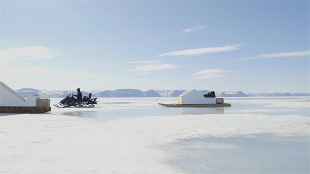 Snowmobile towing a qamutik across sea ice.