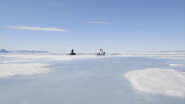 Snowmobiles towing qamutiks across sea ice in the arctic.