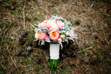 Vintage wedding bouquet with english roses on the ground with cones and dry grass at autumn